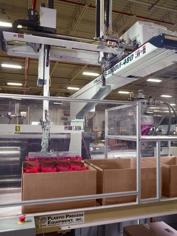 red plastic injection molded parts being stacked into a box in Rodon's facility by an automated arm